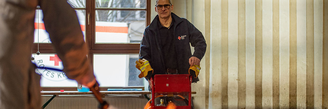 Löschübung mit Feuer im Vordergrund. Lehrgangsteilnehmende Person mit Feuerlöscher löscht das Feuer