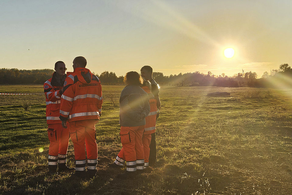 Einsatzkräfte stehen im Sonnenuntergang auf einer Wiese