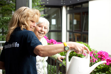 Helferin gießt zusammen mit Seniorin die Balkonblumen