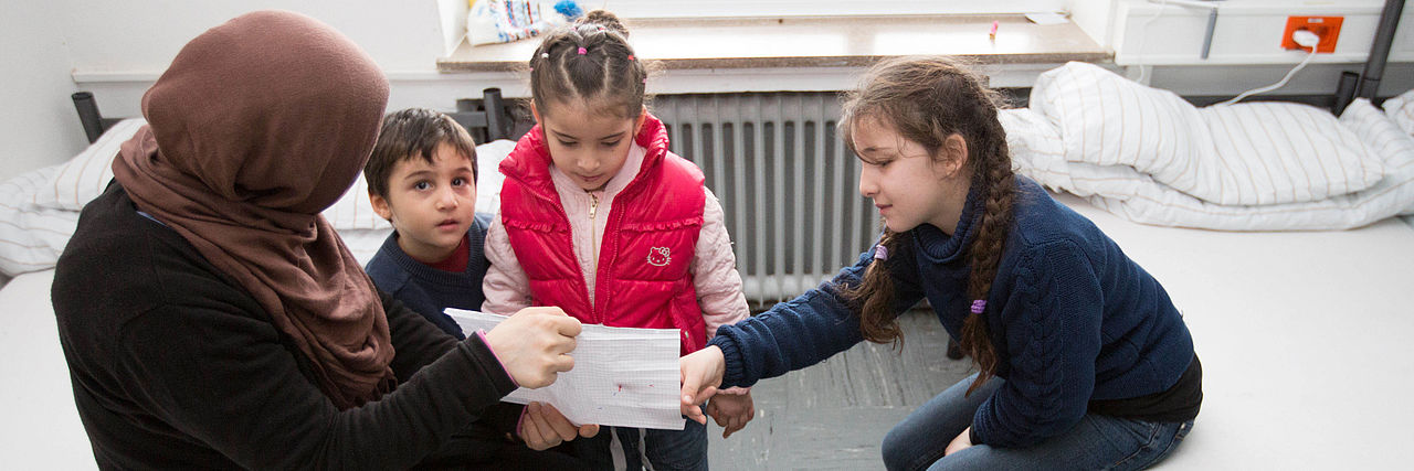 Die Mutter einer geflüchteten Familie schaut sich gemeinsam mit ihren Kindern ein gemaltes Bild an 