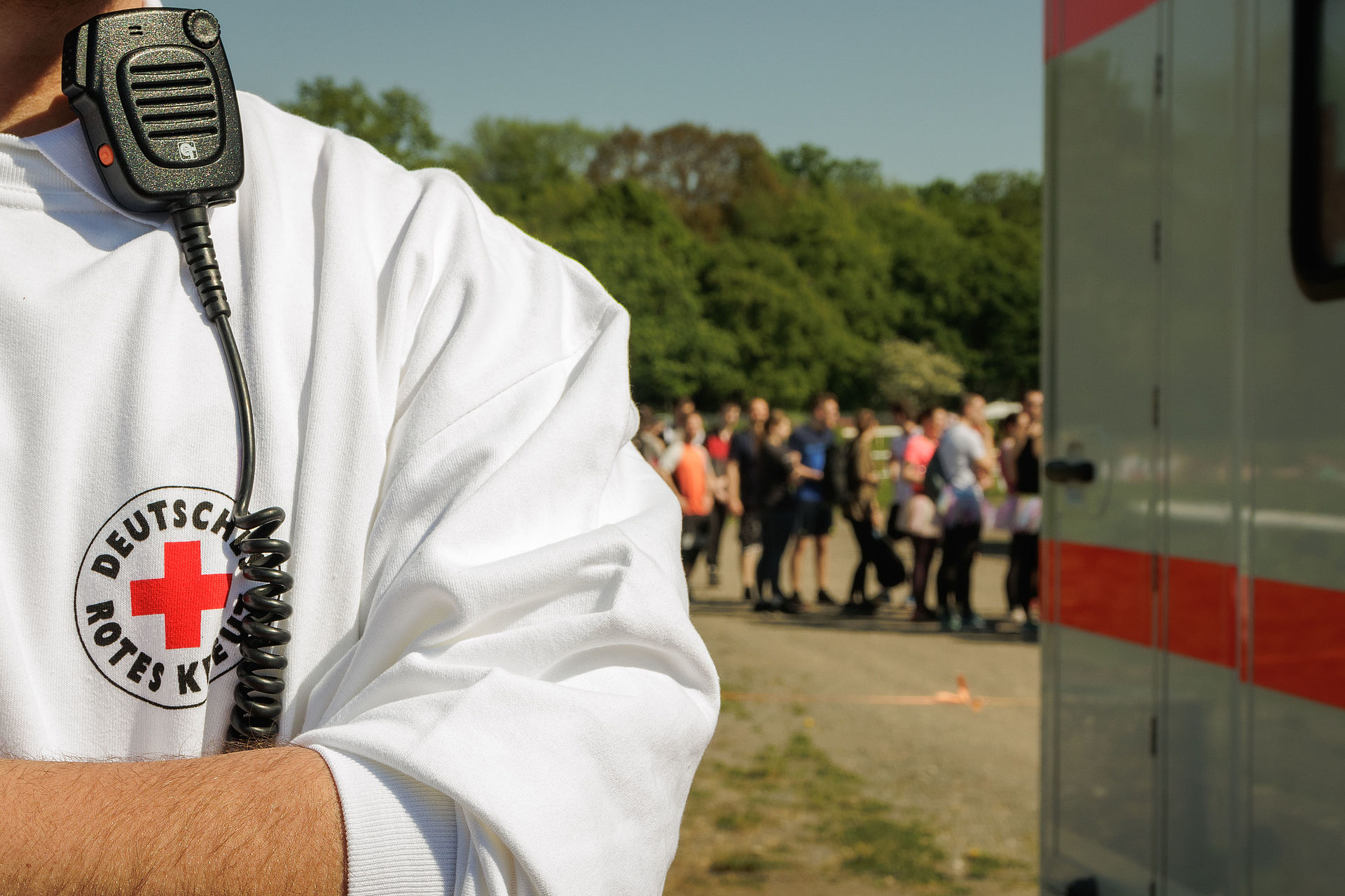 Person angeschnitten im Oberkörper. Mit weißem DRK Polo. Man sieht ein Funkgerät am Körper