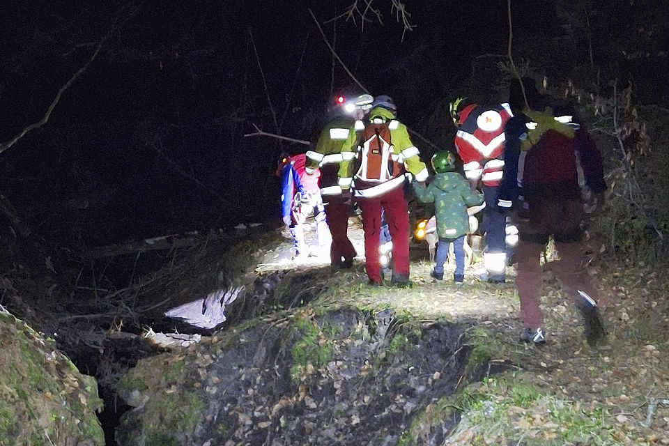 kleiner Junge läuft an der Hand von zwei Rettungskräften durch den nächtlichen Wald