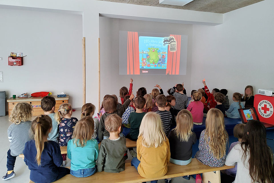 viele Kinder sitzen auf Bänken in einem RAum und schauen einen Film, der mittels Technik an die Wand gebeamt wird