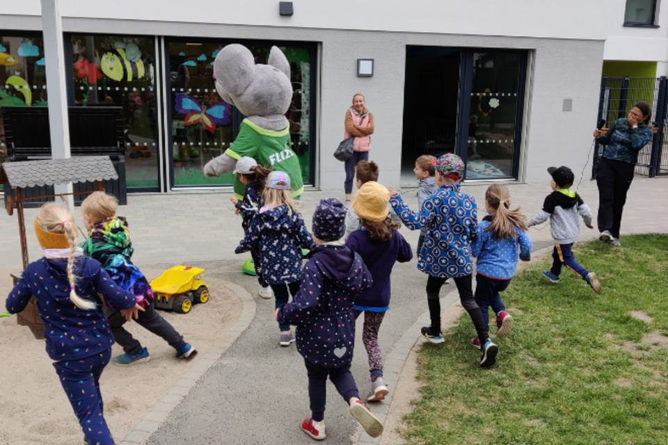 Mehrere Kinder laufen einem Maskottchen hinterher