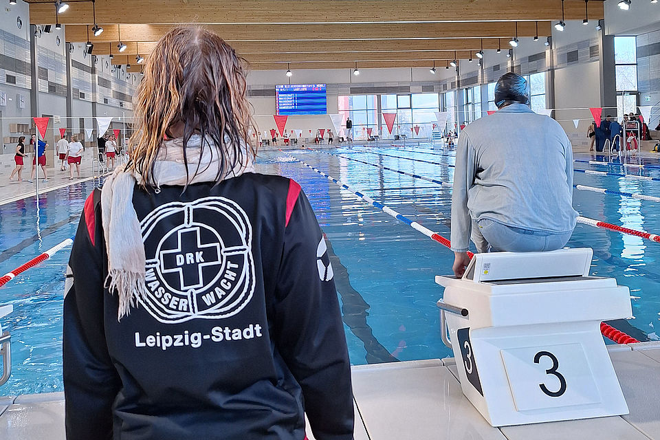 Frau mit nassen Haaren und Wasserwacht-Leipzig-Jacke schaut zu Frau, die auf einem Startblock sitzt