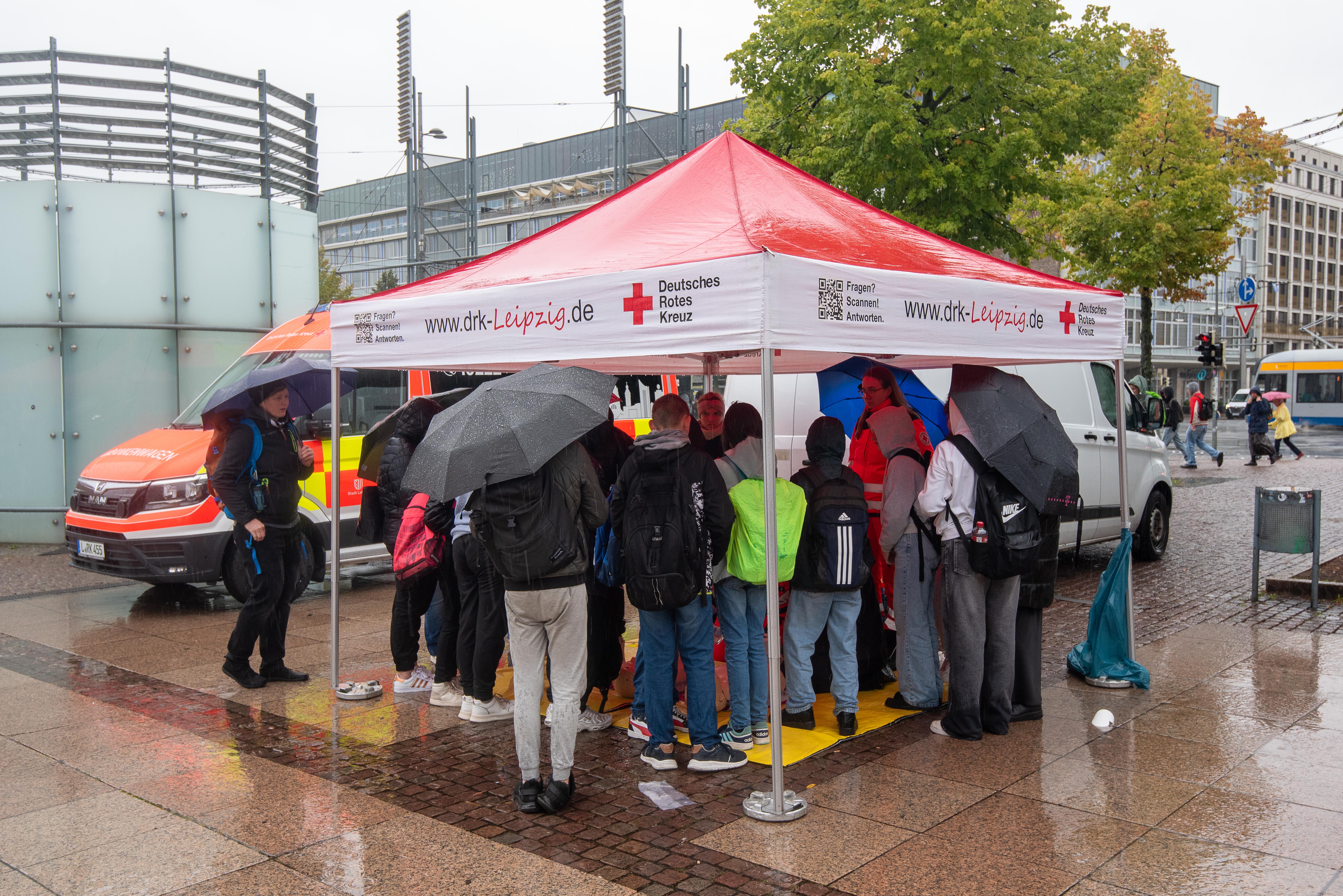 Viele Menschen stehen im Regen unter einem Pavillon und schauen zu, was im Pavillon los ist